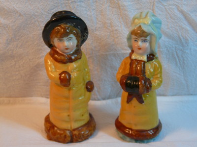 These shakers are more than a hundred years old. They were part of the merchandise that popped up emulating a "Kate Greenaway" design. Kate Greenaway was a children's book illustrator and author who lived during the late 19th century.  Many of her book characters were Victorian children sporting outfits of frilly smocks, mob caps and sunbonnets.