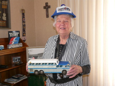 June Unger, is wearing her husband's belt (part of the  Greyhound uniform), and her Greyhound hat. She is holding a toy Greyhound bus, which was a gift from her son Carl.